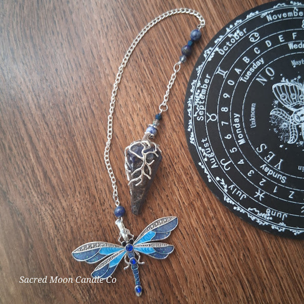 Sodalite and lapis lazuli pendulum with dragonfly charm and chain on wooden surface with black mystical chart