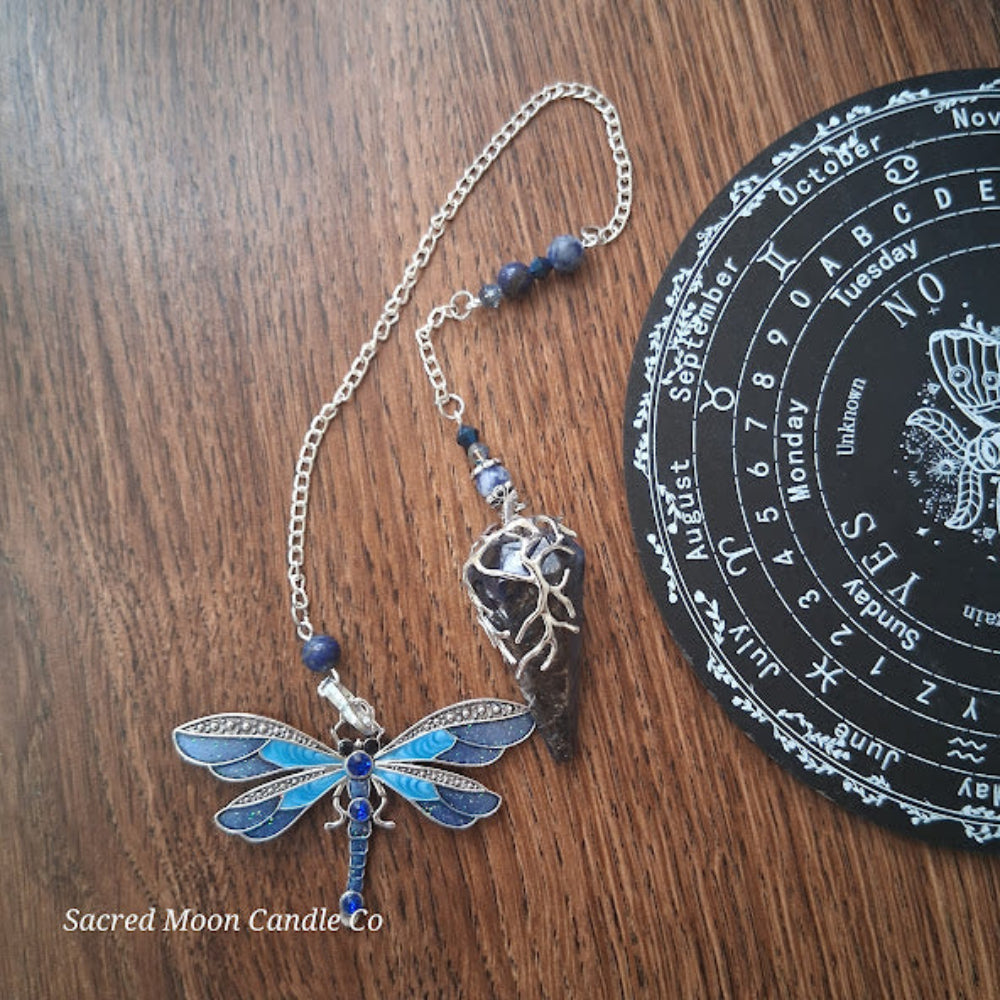 Sodalite and lapis lazuli pendulum with dragonfly charm and intricate silver detailing on wooden surface