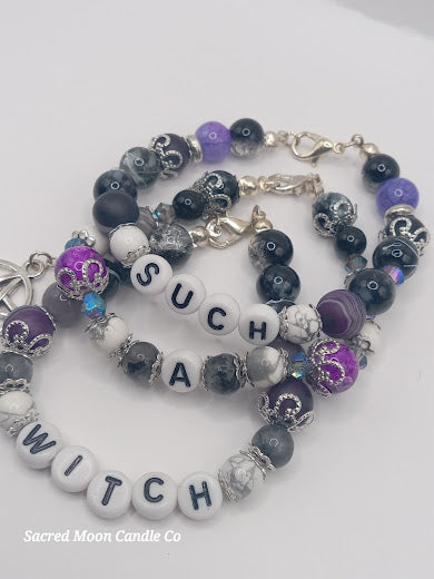 Sacred Moon Candle Co witch bracelet stack featuring black, white, purple beads with letter charms spelling witch