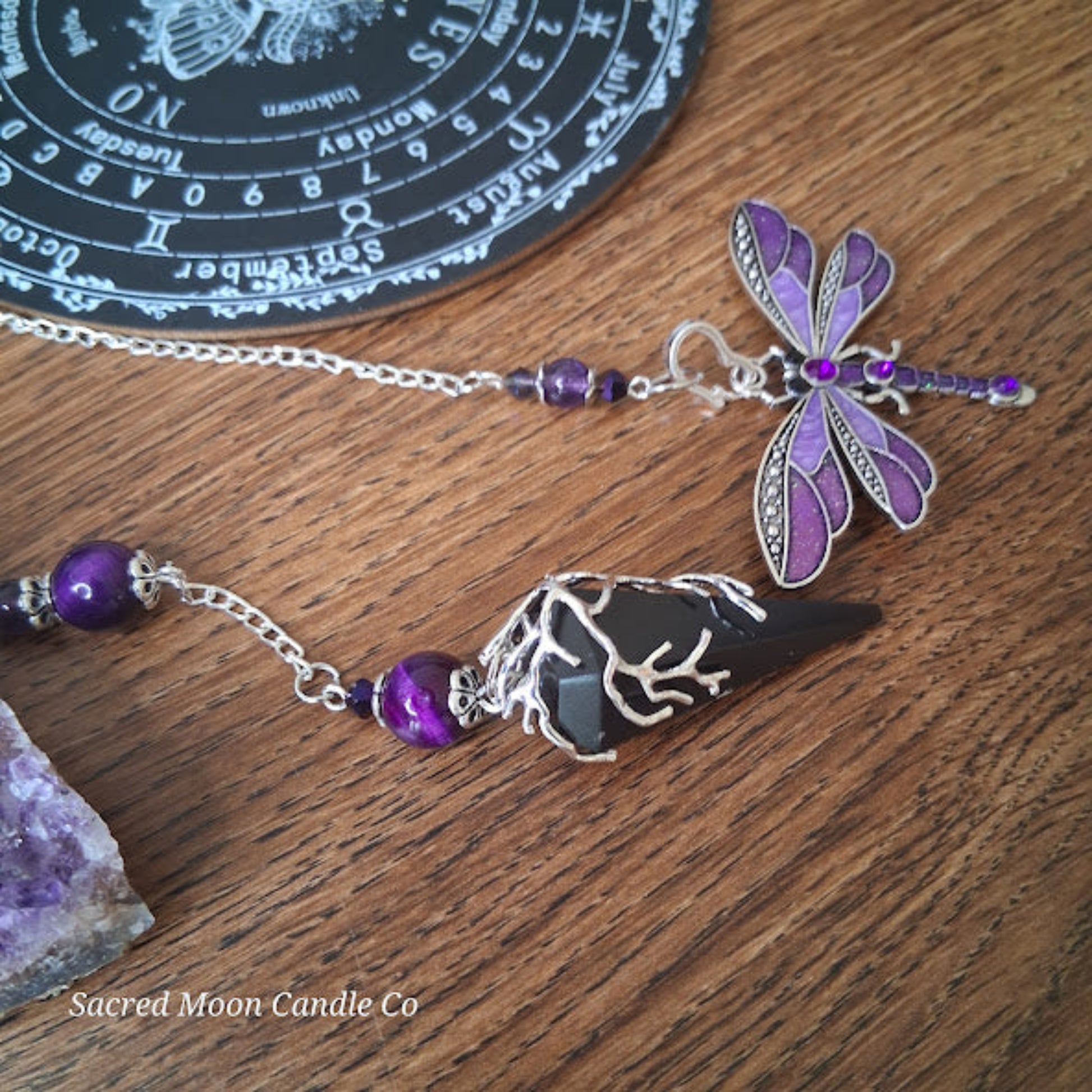 black tourmaline Purple Tigers Eye Dragonfly Pendulum altar tool by Sacred Moon Candle Co on wooden surface