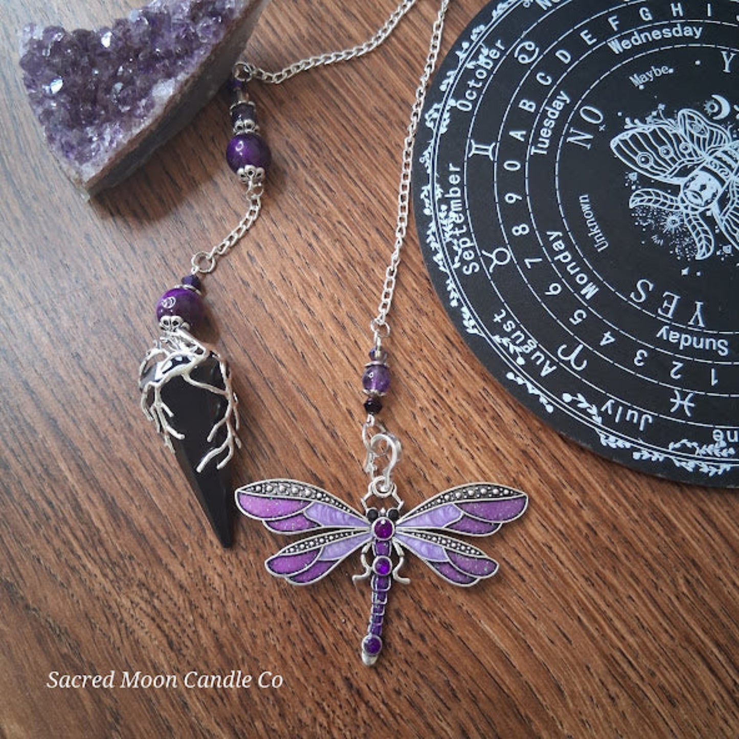 Black tourmaline Purple Tigers Eye Dragonfly Pendulum altar tool on wooden surface with amethyst crystal and astrology board