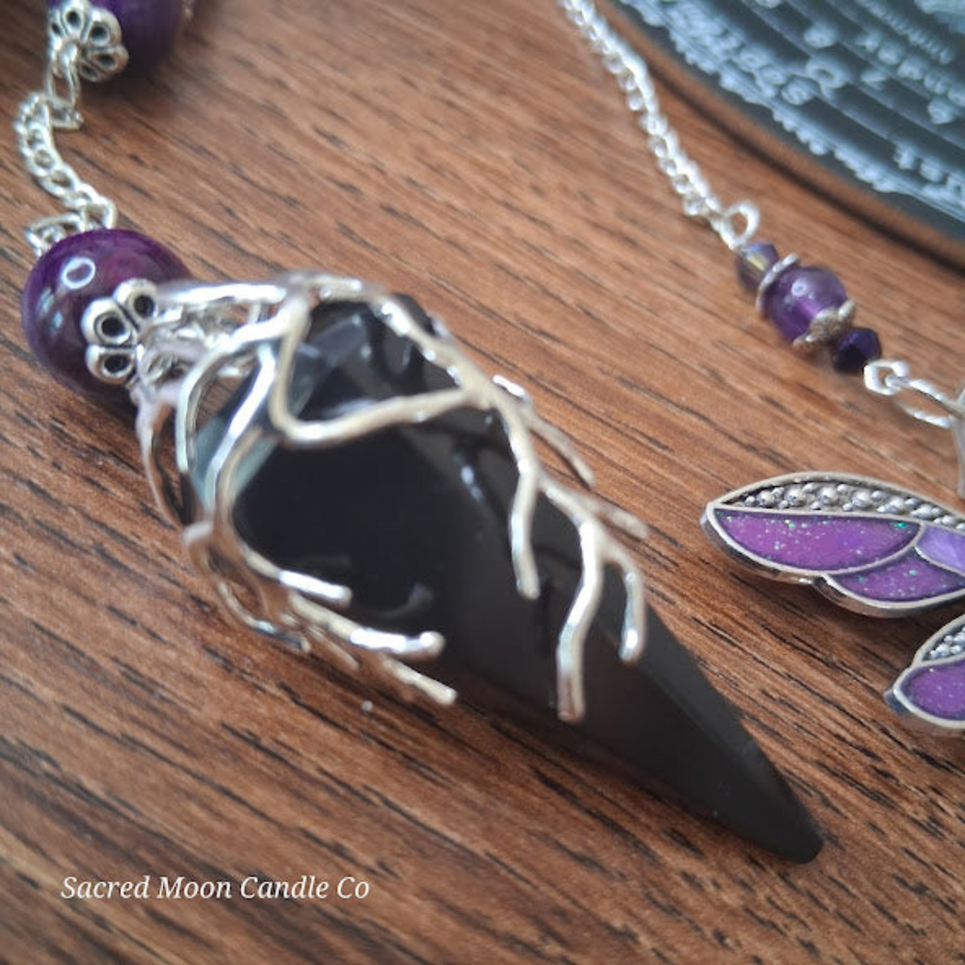 Black tourmaline Purple Tigers Eye Dragonfly Pendulum with silver accents on wooden surface by Sacred Moon Candle Co