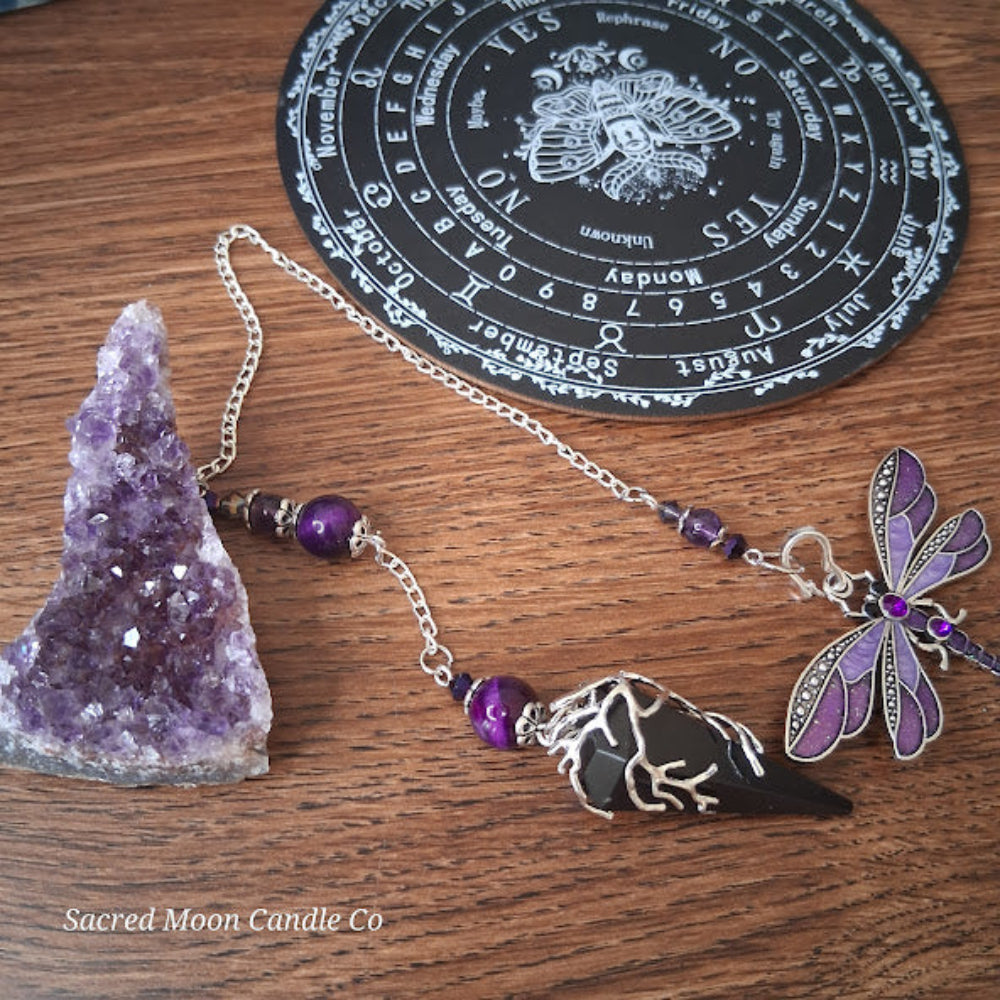 Black tourmaline Purple Tigers Eye Dragonfly Pendulum with amethyst beads on wooden surface next to amethyst cluster
