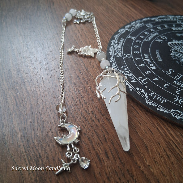 Selenite moon pendulum with silver crescent moon charm and chain from Sacred Moon Candle Co on wooden surface