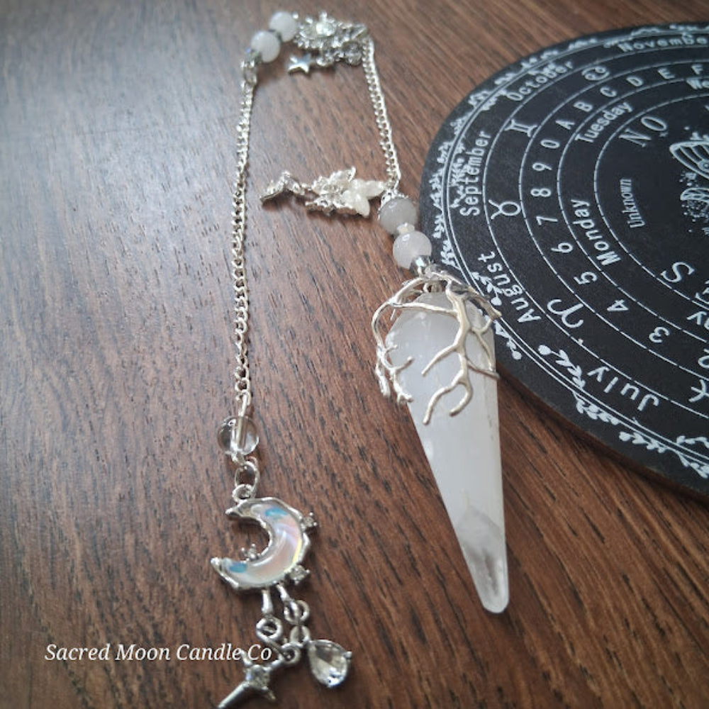 Selenite moon pendulum with silver tree design on wooden surface near a black circular calendar