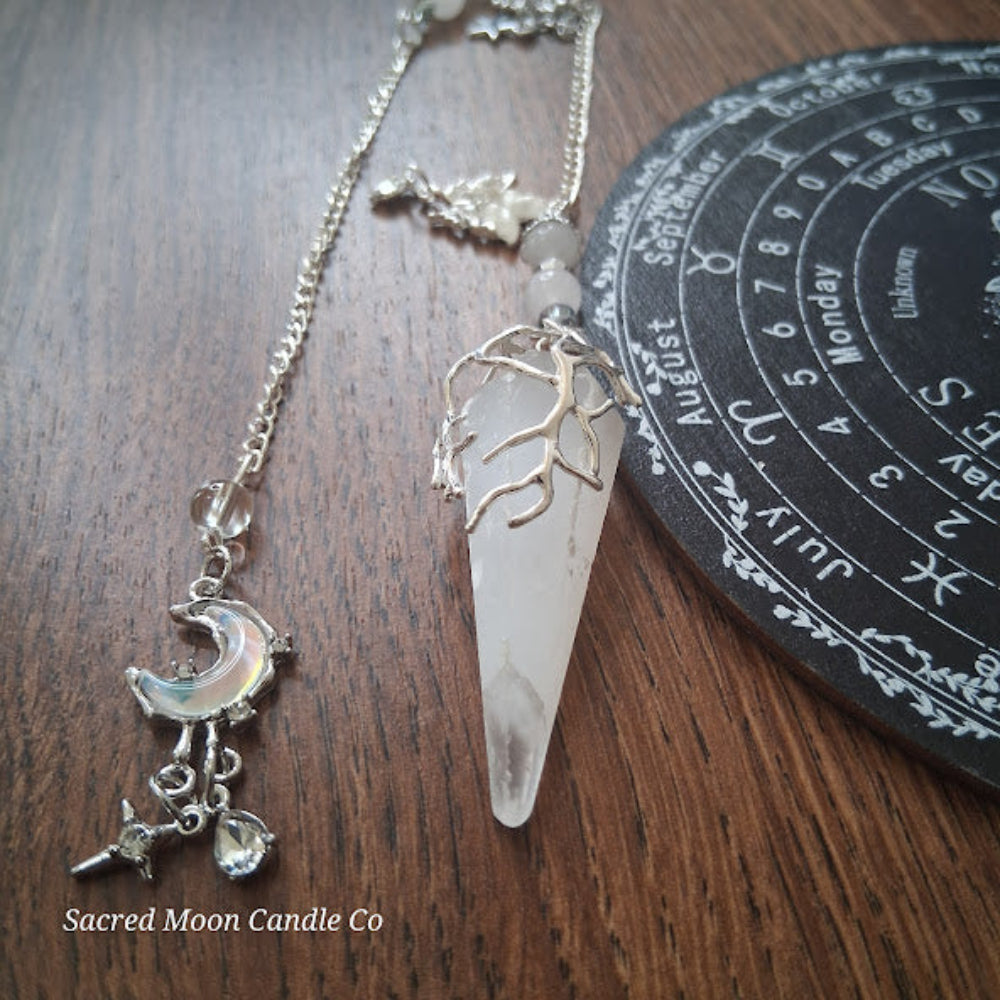 Sacred Moon Candle Co selenite moon pendulum with silver chain and crescent moon charm on wooden surface
