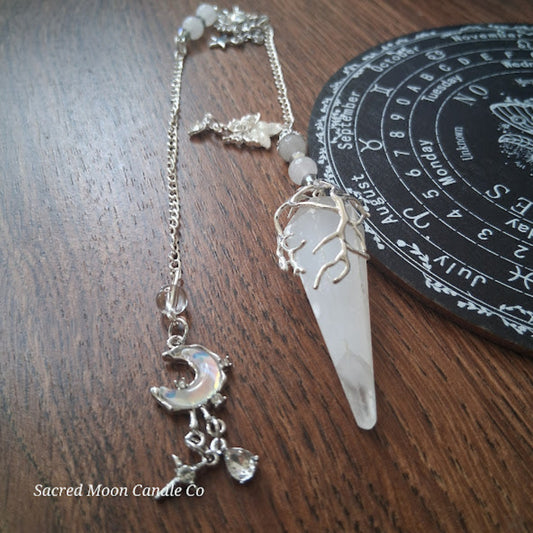 Selenite moon pendulum with silver crescent moon charm and tree design on wooden surface