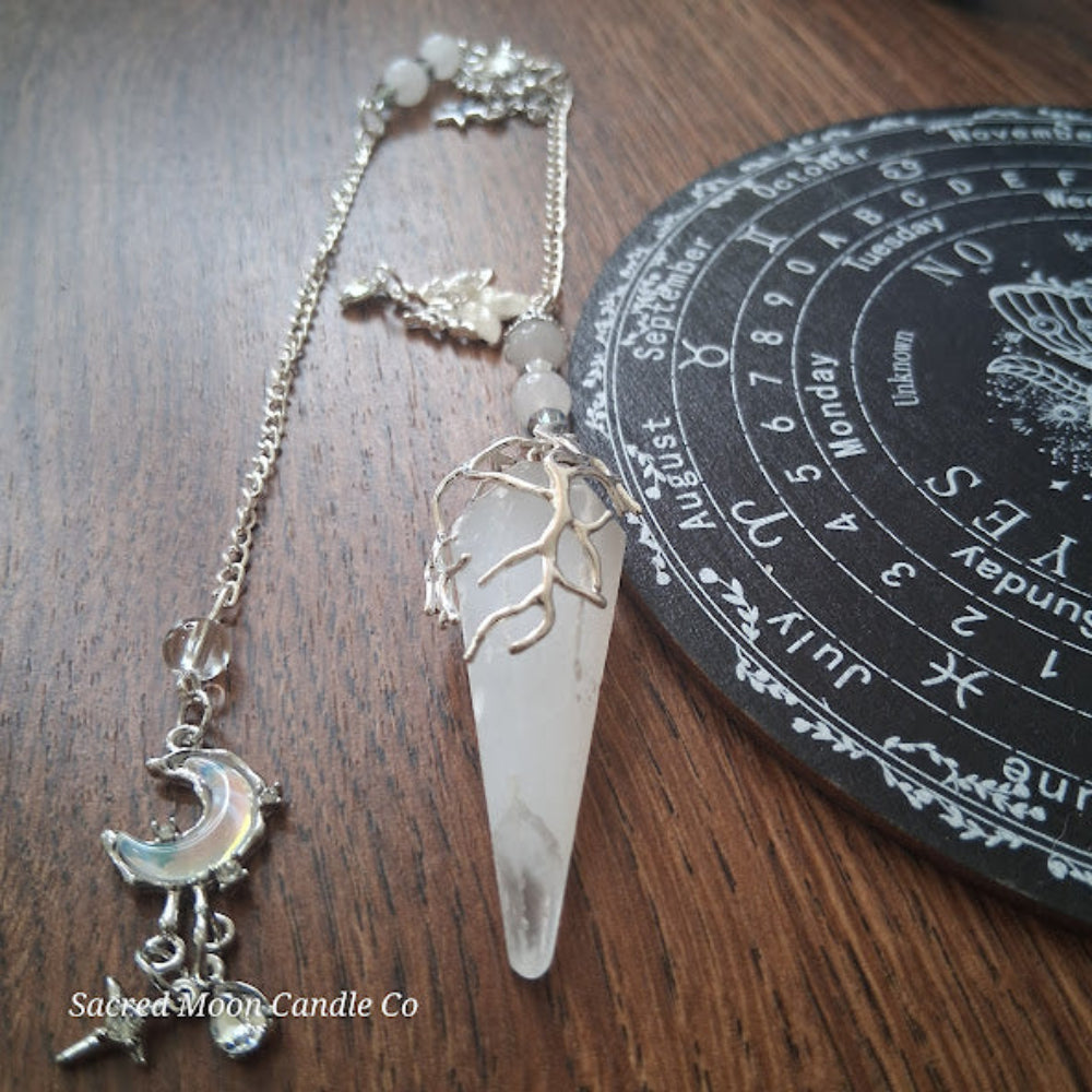 Selenite moon pendulum with silver tree design and moon charm from Sacred Moon Candle Co on wood surface