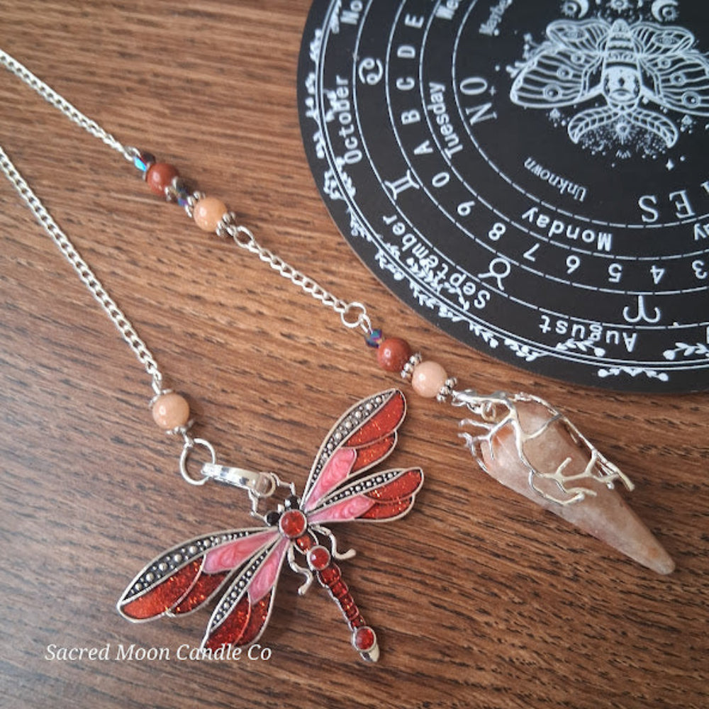 Sunstone dragonfly pendulum for divination with red and pink dragonfly charm and stone pendulum on wooden surface