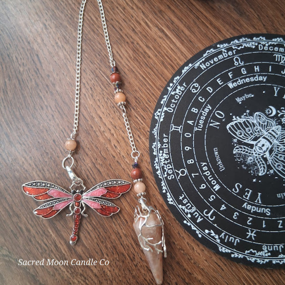 Sunstone dragonfly pendulum for divination with silver dragonfly charm and beaded chain on wood surface