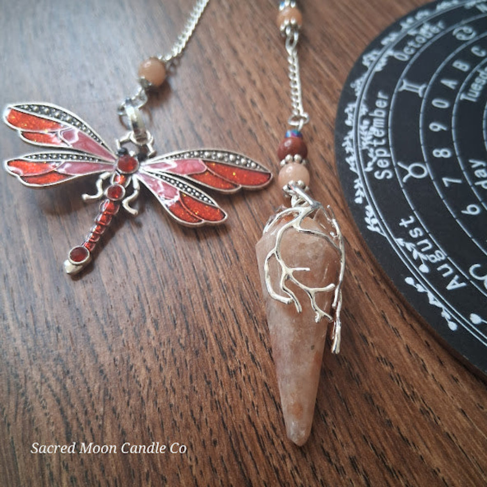 Sunstone dragonfly pendulum for divination with red dragonfly charm and crystal on wooden surface