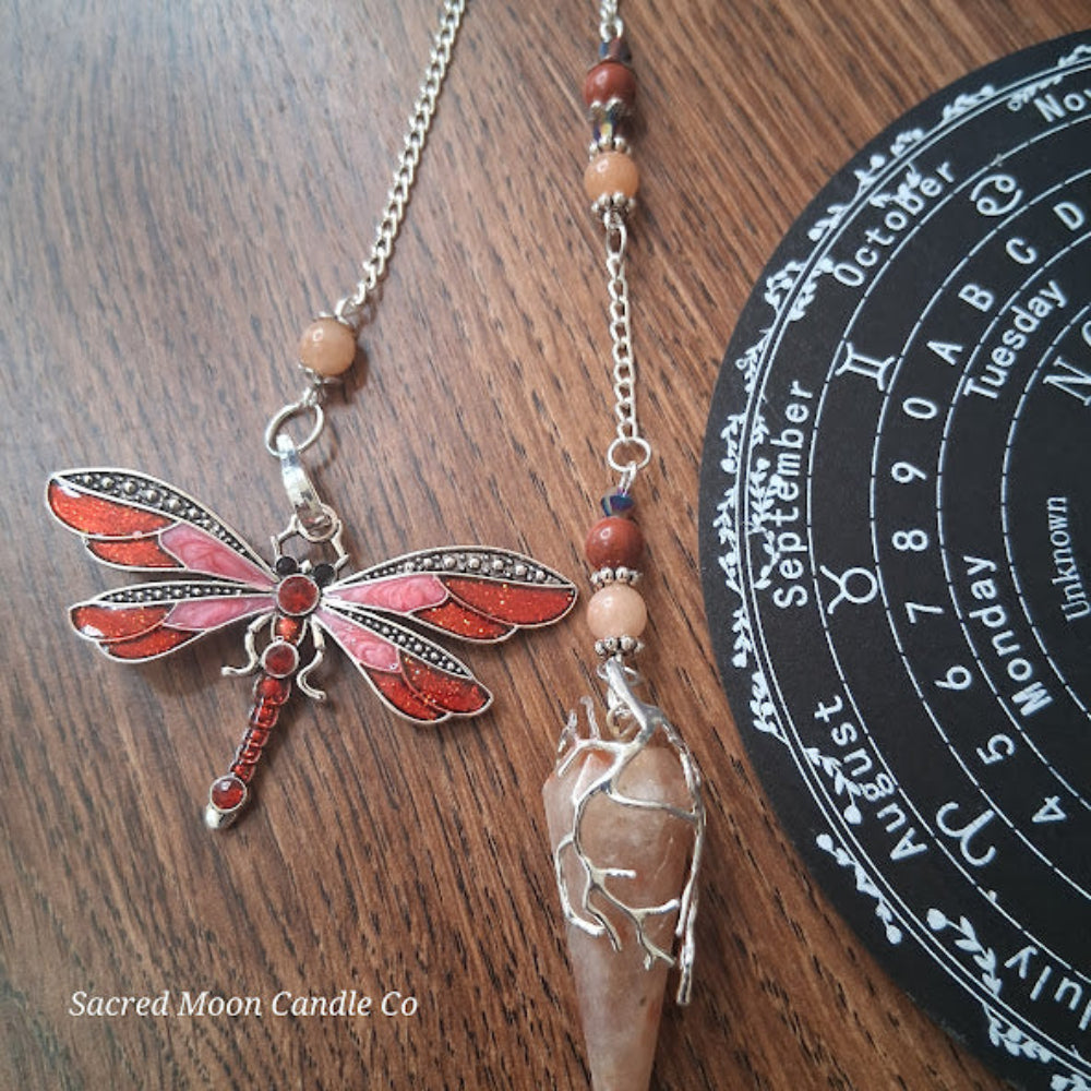 Sunstone dragonfly pendulum for divination with vintage silver and red wings on wooden surface