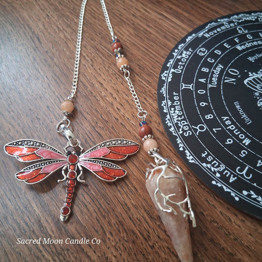 Sunstone dragonfly pendulum for divination with red dragonfly charm and wooden beads on wooden surface