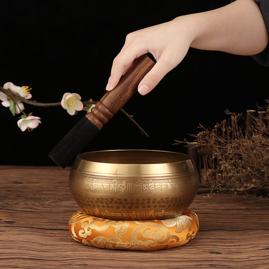 Tibetan Buddha mantra bowl with wooden striker and ornate cushion on wooden surface by Sacred Moon Candle Co