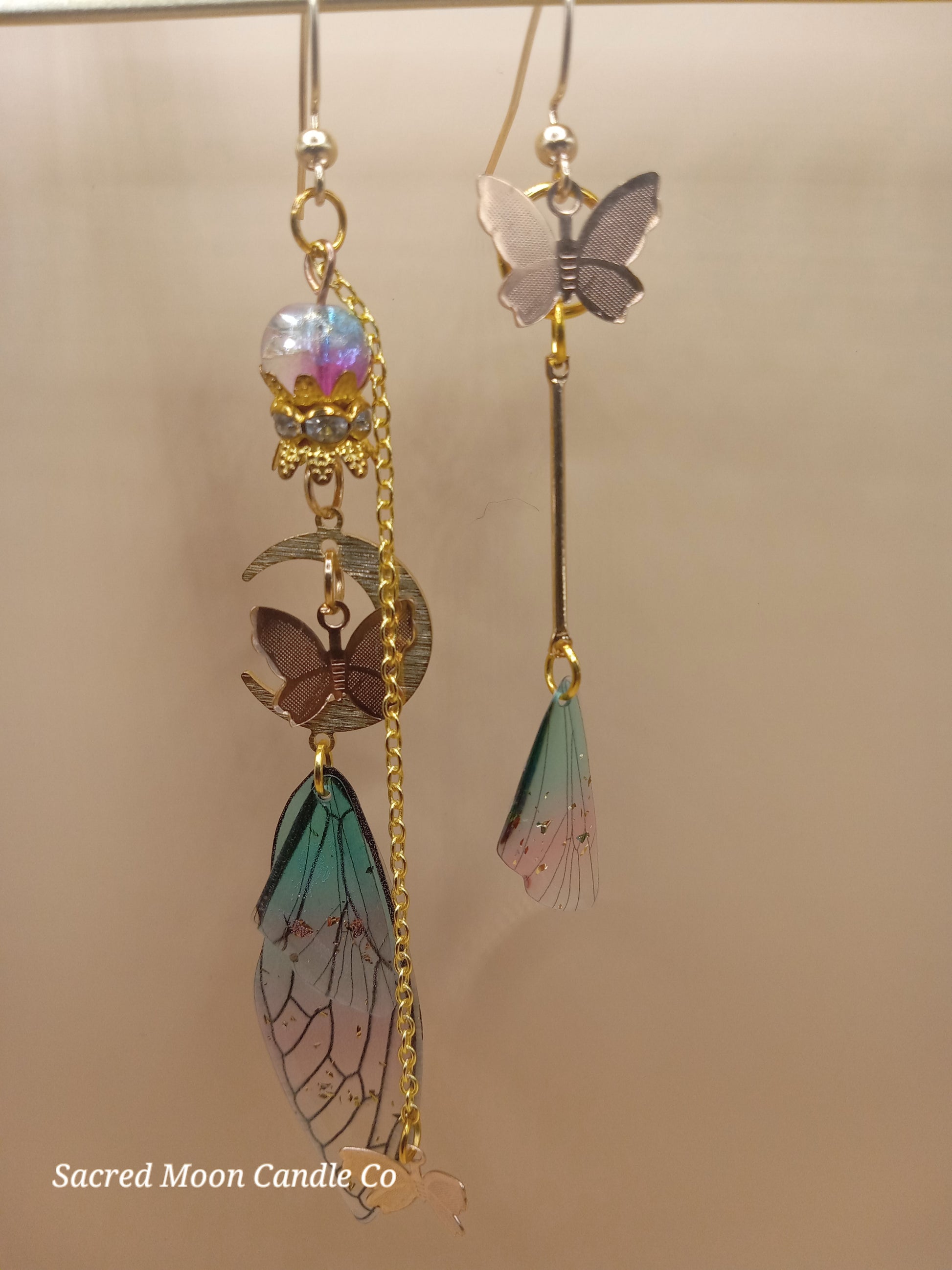 Sacred Moon Candle Co fairy wing earrings with butterfly charms and delicate blue and pink wing details