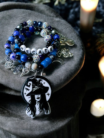 Sacred Moon Candle Co Hecate charm bracelet with blue beads and witch pendant on dark fabric with candles
