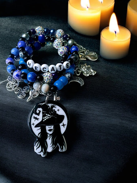 Hecate charm bracelet by Sacred Moon Candle Co featuring blue beads and witch pendant near candles