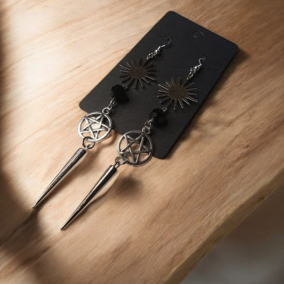 Sacred Moon Candle Co sunburst pentacle earrings with spike dangles on black display card