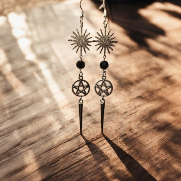 Sacred Moon Candle Co sunburst pentacle earrings with black beads and dangling spikes on wooden background