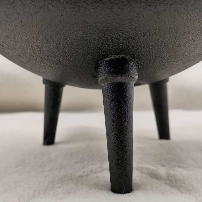 Close-up of three-legged cast iron cauldron legs by Sacred Moon Candle Co on white surface